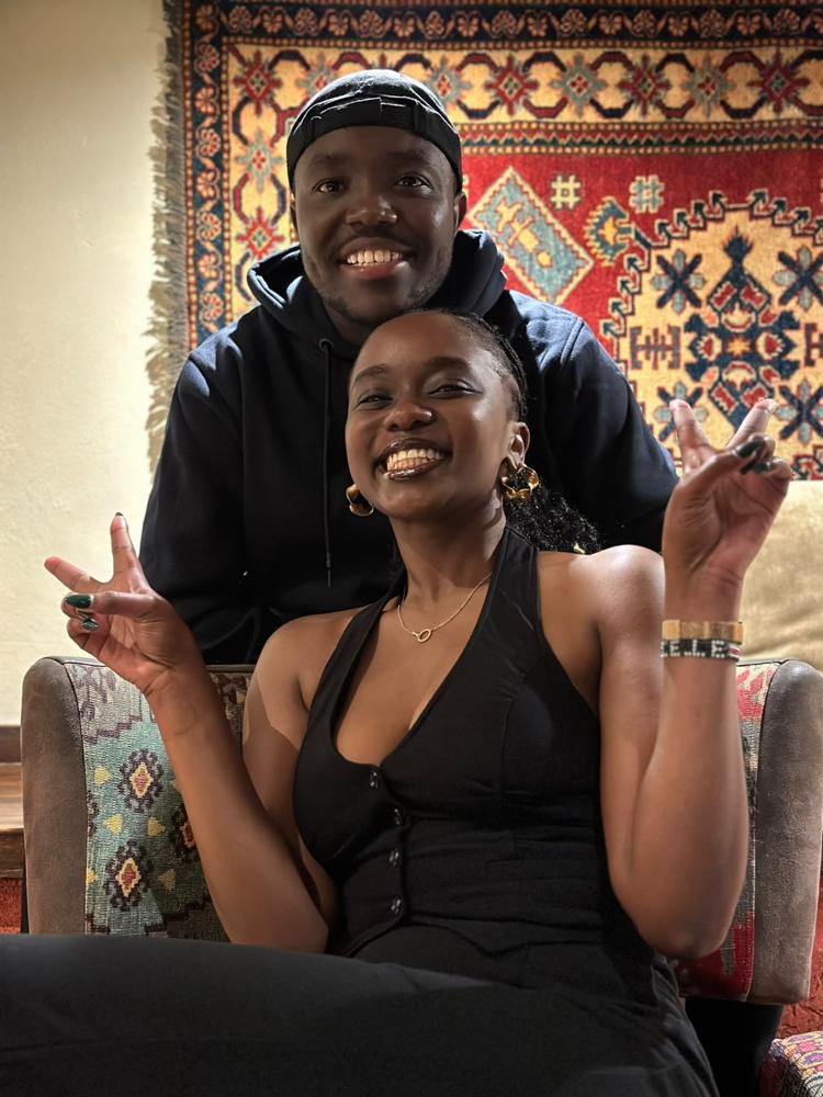 Tete and Ian in front of a red woven tapestry