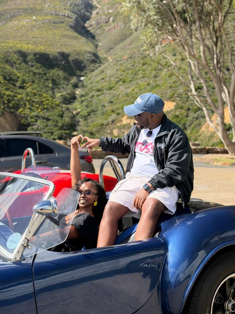 Ian and Tete holding hands in a roadster